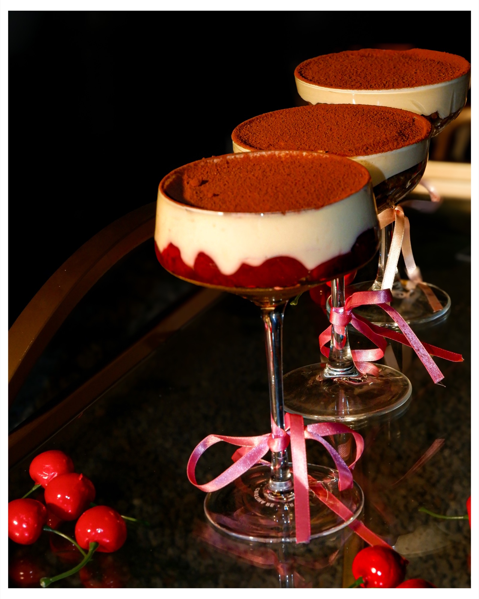 Three cherry tiramisu desserts in ribbon-tied coupe glasses, photographed by MJ