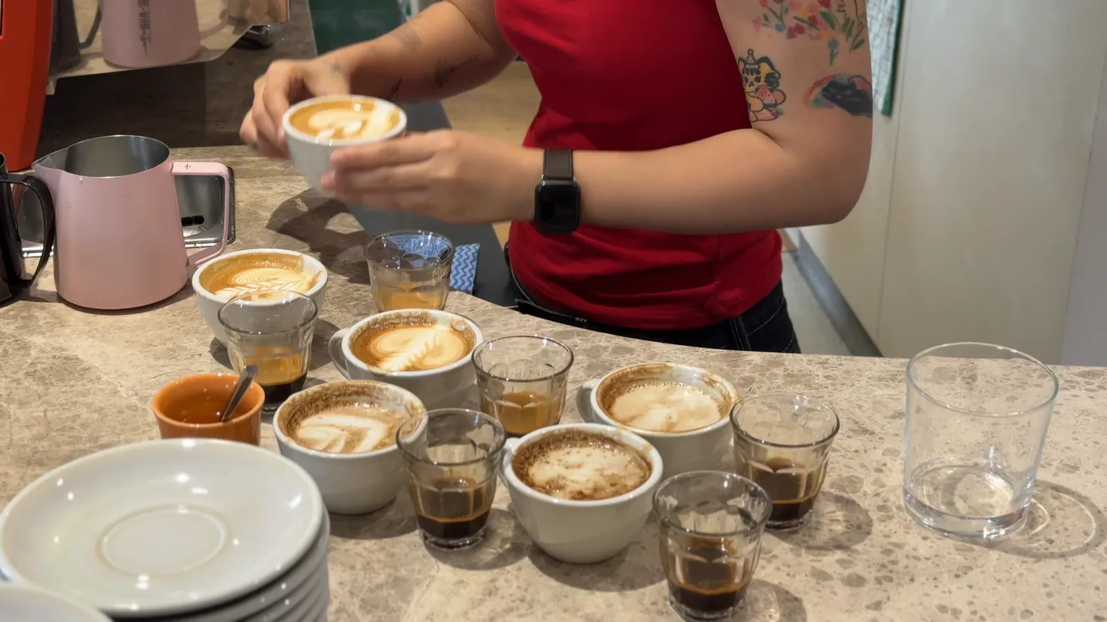 A counter of latte cups and espresso glasses after the morning taste test at FAVE, with a barista lifting one cup