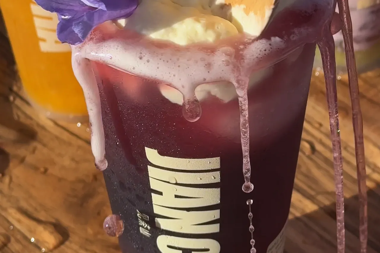 A purple drink with cream cheese and jacaranda petals on top, spilling over the rim and down the Jian Cha cup