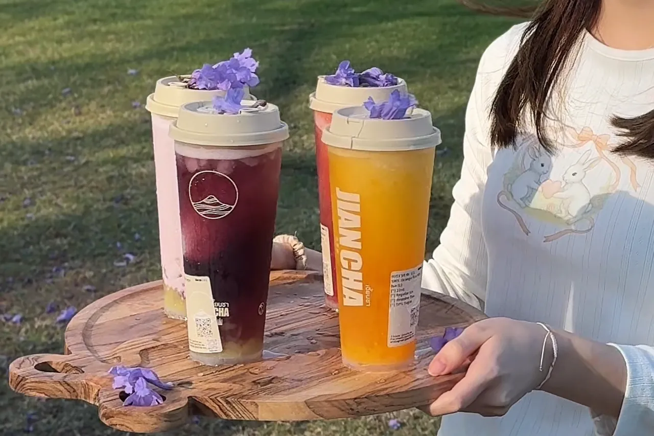Four Jian Cha drinks topped with jacaranda petals, carried on a wooden tray across the grass in New Farm Park